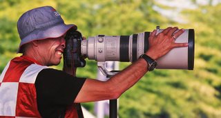 man wearing a hat taking a photo with a camera with a massive lens
