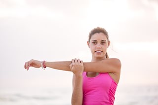 young woman in pink top stretching her arm