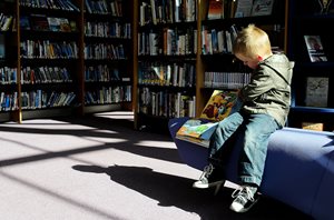 kid sitting on a bench reading a book in a library