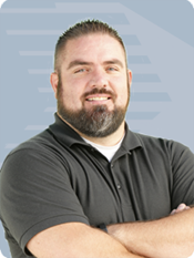 Muscular man with full beard wearing a dark polo with his arms crossed, smiling