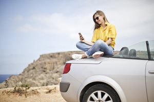 Young woman sitting on back of car looking at a phone at the beach