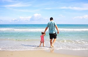 Father walking with toddler daughter on the sandy beach