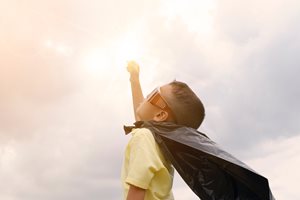 young boy with cape and sunglasses up pretending to fly