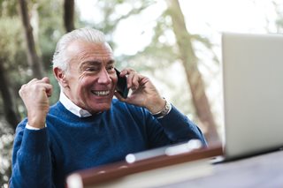 old man happy on the phone looking at a laptop