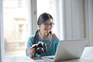 Asian woman holding a camera looking at a laptop