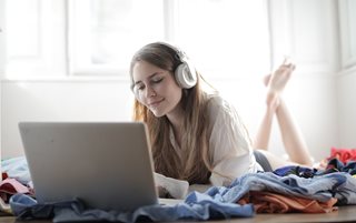 woman laying on bed using laptop with headphones