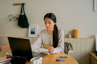 woman sitting at kitchen table with computer and credit card