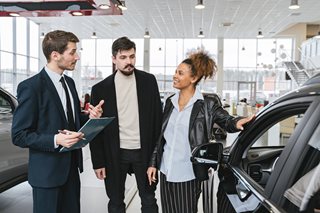 two people and a car salesman talking next to a new car