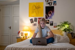 blonde teenager looking at laptop on bed