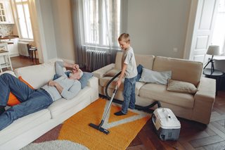 old man laying on couch while child vacuums a rug