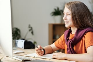 young teen girl writing and looking at computer