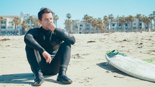 man in wet suit next to surfboard