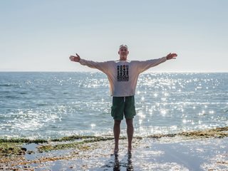 bald man with arms out on beach