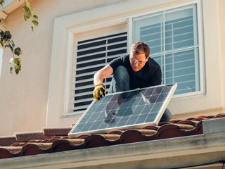 man installing a solar panel on a roof