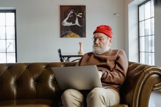 old man with red hat typing on laptop