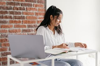 teenage girl looking at books with laptop next to her