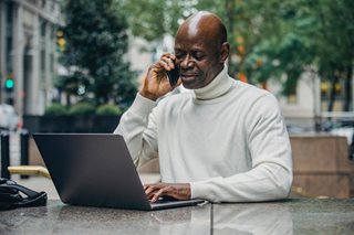 bald man in turtleneck on the phone and looking at laptop
