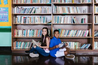 two kids sitting back to back at a library