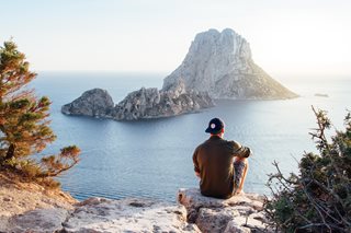man sitting on a cliff looking over some water