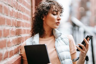 woman looking at a phone leaning against a brick wall
