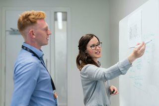 woman writing on white board while a man looks