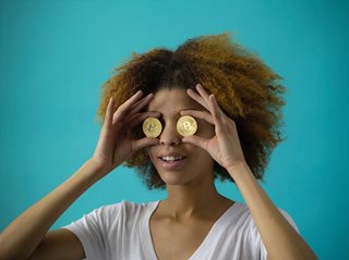 black woman holding up bitcoins up to her eyes