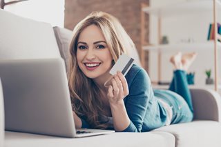 smiling woman holding a debit card looking at a laptop