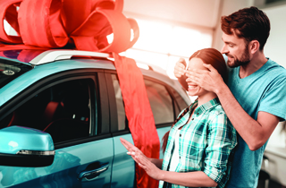 man covering woman's eyes next to a car with a giant bow on it